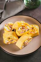 Mini tortilla rolls with chopped sausages, cheese, eggs and herbs on a plate vertical view photo