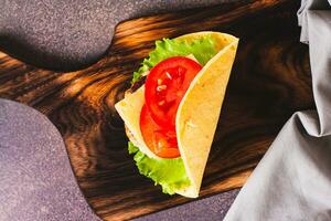 Close up of taco burger with cutlet, cheese and tomatoes on a board on the table top view photo