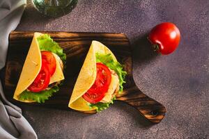 Taco burger with cutlet, cheese and tomatoes on a board on the table top view photo