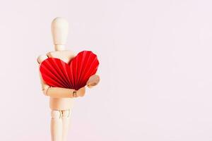 Wooden man holding a big red origami heart on a pink background photo