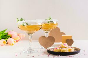 Sweet cocktails with rosemary in glasses and candy hearts on a plate for Valentine's day photo