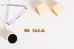 Concept be calm word, cup of coffee, notepad and glasses on a light background top view photo