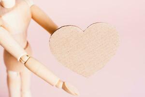 Craft cardboard heart in wooden hands on a pink background copy space photo