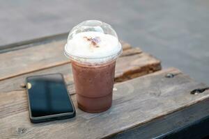 Iced coffee, iced cocoa in clear plastic cups near the black smartphone on an old wooden table in a relaxing corner coffee shop. copy space photo