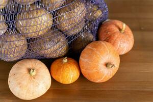 Harvest Season, Fresh Potatoes and Ripe Pumpkins in Mesh Bag on Wooden Table photo