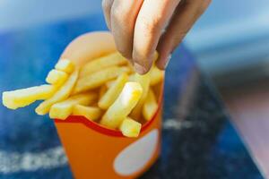 the child's hand takes a delicious golden French fries from a paper cup photo