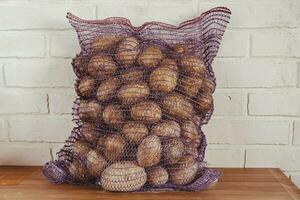 Harvested Fresh Potatoes in Mesh Bag on Wooden Table for Food Supply photo