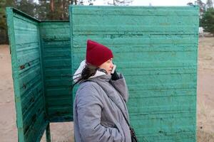 Portrait of Woman Wearing Autumn Clothes, Talking on Phone in Vintage Beach Changing Booth photo