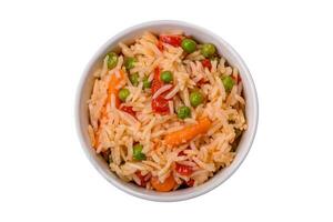 Delicious boiled rice with vegetables peppers, green peas, salt, spices and herbs photo