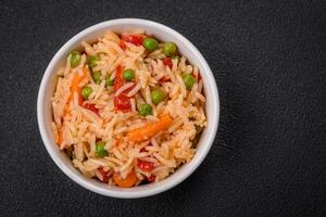 Delicious boiled rice with vegetables peppers, green peas, salt, spices and herbs photo