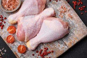 Raw chicken legs with salt, spices and herbs on a dark concrete background photo