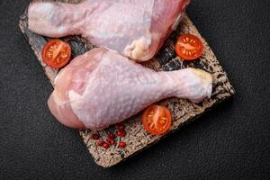 Raw chicken legs with salt, spices and herbs on a dark concrete background photo