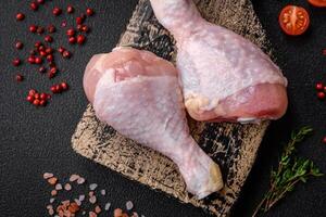 Raw chicken legs with salt, spices and herbs on a dark concrete background photo