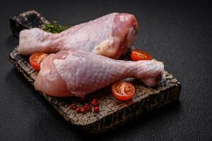 Raw chicken legs with salt, spices and herbs on a dark concrete background photo