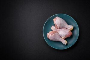 Raw chicken legs with salt, spices and herbs on a dark concrete background photo