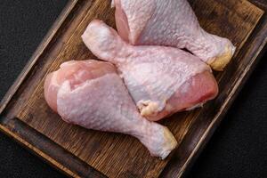 Raw chicken legs with salt, spices and herbs on a dark concrete background photo