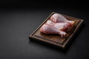 Raw chicken legs with salt, spices and herbs on a dark concrete background photo