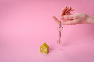 Female hands, a small wooden house and keys as an idea for investing in your own home and achieving the goal of buying real estate photo