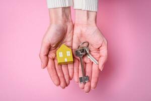 Female hands, a small wooden house and keys as an idea for investing in your own home and achieving the goal of buying real estate photo