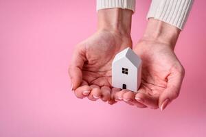 Female hands, a small wooden house and keys as an idea for investing in your own home and achieving the goal of buying real estate photo