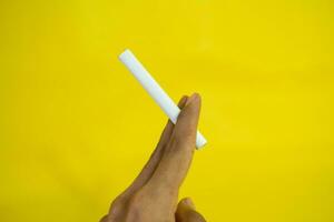 A man hand holds a handmade cigarette on yellow background photo