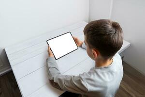 Boy hold tablet with isolated screen for game or app promotion on a tidy work desk. Perfect for showcasing digital entertainment and educational applications photo