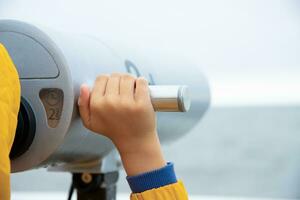 the boy looks through binoculars at the Baltic Sea. cool weather. photo