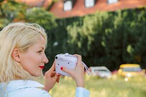 a woman on the street takes pictures on a polaroid. a warm summer day. view from the back photo