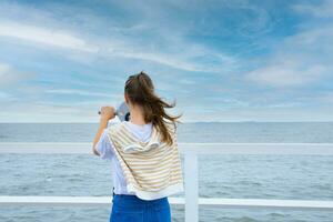 A young woman looks through coin binoculars, rear view. baltic sea, cold weather photo