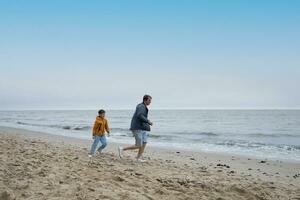 dad and his son are having fun running on the autumn beach. cool weather. photo