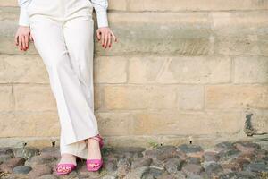 A young woman in white trousers, pink shoes, stands near a brick wall. Fashion, style. copy space. summer photo