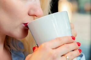 de cerca foto de un joven mujer Bebiendo caliente café o té en un café o a hogar. rojo lápiz labial