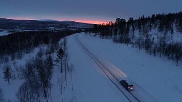 antenn bil körning längs snöig berg motorväg genom tall skog på solnedgång video