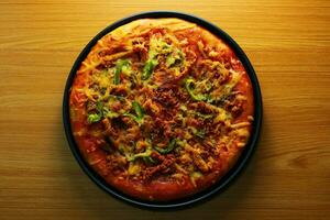 Pizza with meat and vegetables in a black plate on a wooden table photo