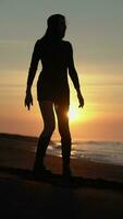 smal kvinna gående och vändning runt om på sandig strand på soluppgång. kvinna i sommar kort klänning, stövlar video