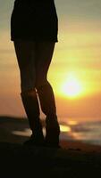 Slender female legs in high boots walking beach on background of sun rising above horizon at sunrise video