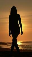 silhouette sottile donna a piedi su sabbioso spiaggia a Alba. femmina con lungo gambe nel corto vestito video
