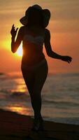 Sensuality woman in bikini walking on beach at sunrise on background solar disk rising above horizon video