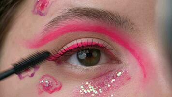 Female eye with make-up with pink sparkles and arrows paints false eyelashes in front of mirror video