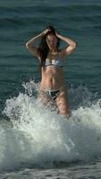lleno longitud mujer en bikini en pie en playa en agua de salpicaduras rotura olas de Pacífico Oceano video