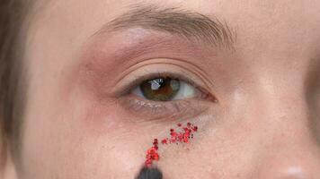 Make-up brush applies red sparkles to face of female model with brown eyes and looking at camera video