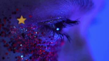 Extreme close-up view of women eye with shiny makeup with sparkles illuminated blue-pink neon light video