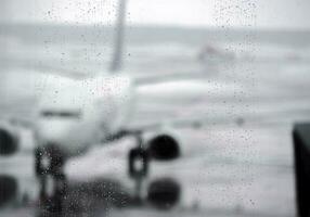 borroso imagen monocromo de gotas de lluvia en terminal del aeropuerto ventanas con blanco avión en lluvia mojado pista antecedentes. foto