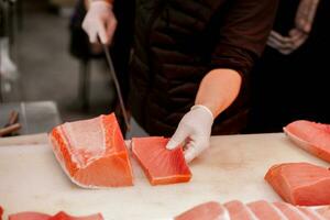 manos de japonés cocinero utilizando cocinero cuchillo rebanado pedazo de Fresco atún pescado para vender a cliente en Mañana pescado mercado, Japón. foto