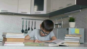 un chico con lentes lo hace deberes utilizando muchos libros de texto y libros. retrato de un colegial video