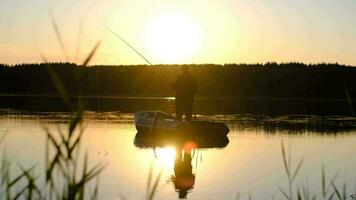 fiske på hav, fiskare i en båt, fiske under solnedgång, aktiva resten. en man i en keps är fiske medan stående i en båt under solnedgång. Sol blossa video