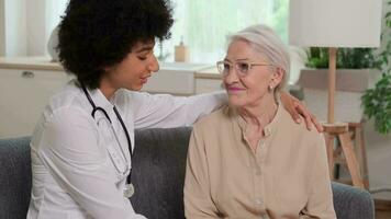 afro americano donna medico auguri bene per un' anziano donna mettendo sua mano su sua spalla. famiglia medico, paziente sostegno, Aiuto a casa, cura per il malato. video