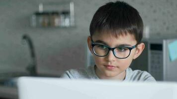 portrait de une écolier dans des lunettes qui est en train d'étudier en utilisant en ligne La technologie et une portable séance à Accueil à le table video