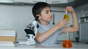 Close-up. An attractive schoolboy teaches chemistry using a microscope and flasks with liquid and makes notes in a notebook. Homework. video