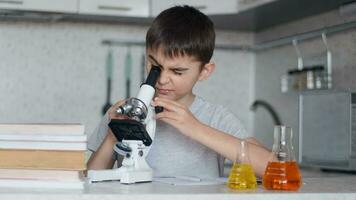 attraente ragazzo insegna chimica utilizzando un' microscopio e fa Appunti nel un' taccuino. compiti a casa video